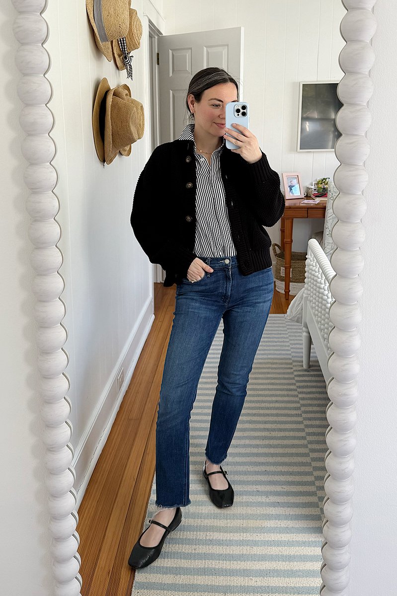 Carly Riordan taking a mirror selfie wearing a black cardigan and mary janes. 