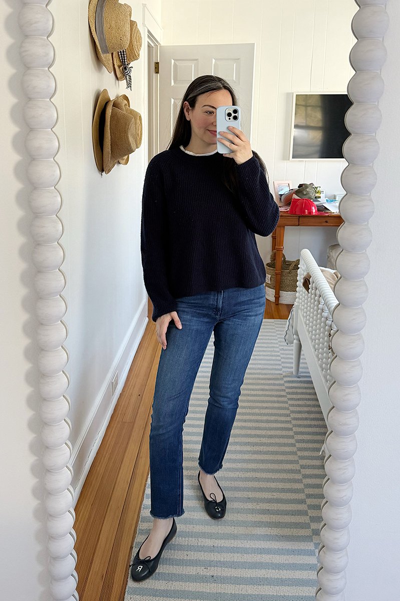 Carly Riordan taking a mirror selfie wearing a navy sweater and jeans.