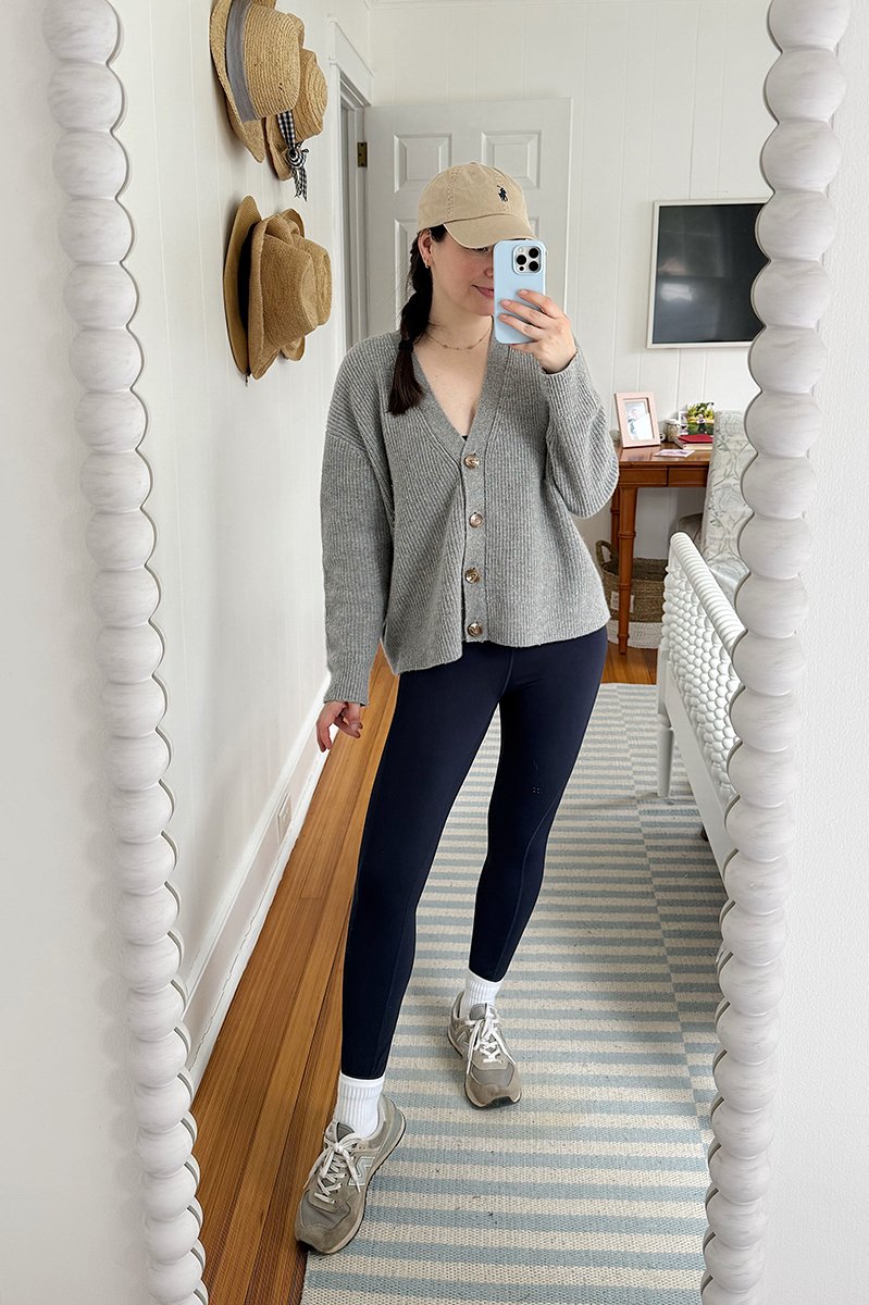 Carly Riordan taking a mirror selfie wearing a grey cardigan and sneakers.