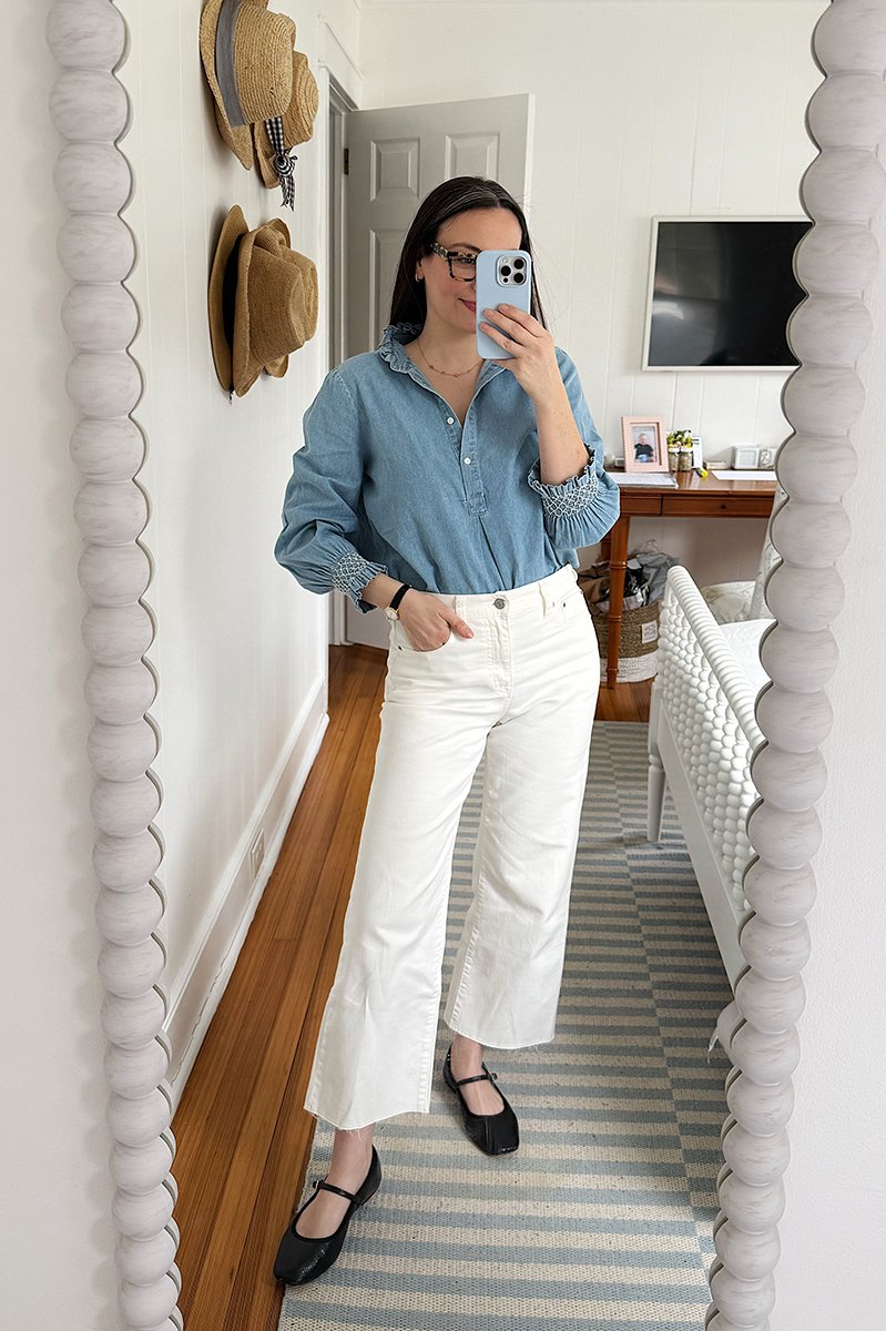 Carly Riordan taking a mirror selfie wearing a chambray shirt and white jeans.