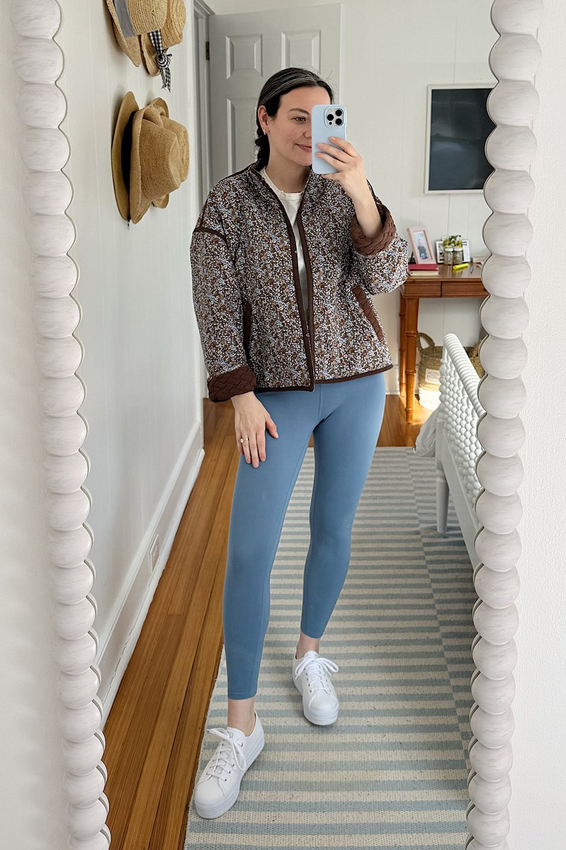 Carly Riordan taking a mirror selfie wearing a reversible quilted jacket and leggings.